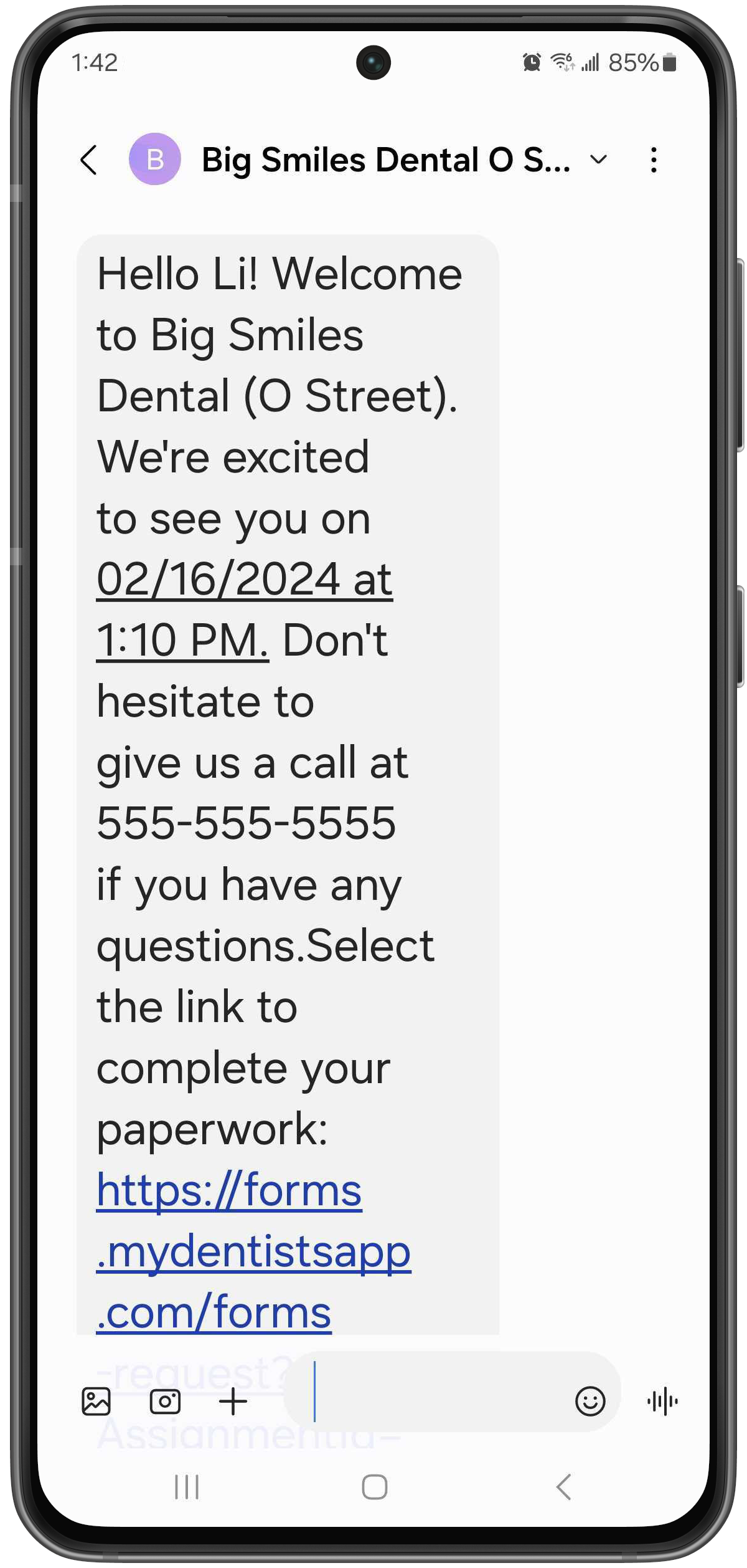 Phone with a text that reads "Hello Li! Welcome to Big Smiles Dental. We're excited to see you on February 16, 2024 at 1:10PM. Don't hesitate to give us a call at 555-555-5555 if you have any questions. Select the link to complete your paperwork." A link is then listed.
